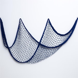 Puede incluir: Una red de pesca decorativa azul marino, suspendida sobre un fondo blanco. La red est&aacute; hecha de cuerda tejida, con un patr&oacute;n de malla en forma de diamante. Dise&ntilde;ada para colgar como decoraci&oacute;n de pared.