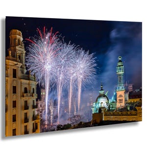 May include: A night-time view of a city skyline with fireworks exploding over a building with a dome. The building is lit up with lights and the fireworks are a bright white and blue.
