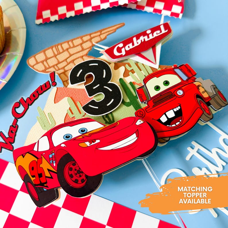May include: Cars themed cake topper featuring Lightning McQueen and Mater, a red race car and a red tow truck, with a black number 3 and a red sign that says "Gabriel".