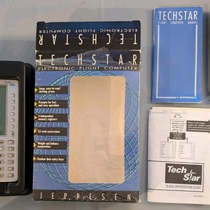 May include: A Jeppesen Techstar electronic flight computer set including a silver handheld device in a black tray, a blue and white product box, a blue manual, a white quick orientation guide, and a black protective carrying case.