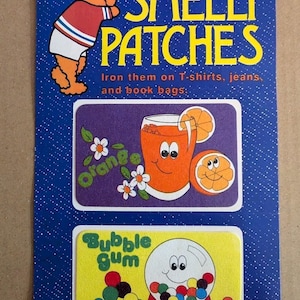 May include: A blue cardboard backing card with white dots features two Sniffys iron-on patches. One patch shows an orange juice glass with an orange slice and the text Orange. The other patch shows a gumball machine with the text Bubble gum.