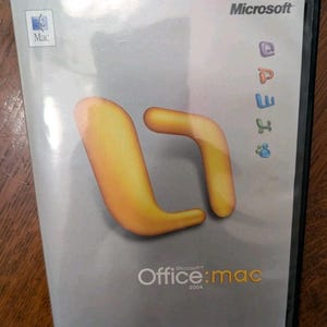 May include: A silver software box for Microsoft Office 2004 for Mac. The cover features a large, abstract orange graphic, the Microsoft logo, a Mac logo, and four small colorful icons. The text reads Microsoft Office:mac 2004 in white and yellow.