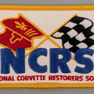 May include: A rectangular embroidered patch with a white background and a yellow border. It features a red emblem and a black and white checkered flag crossed above the blue text NCRS and the red text NATIONAL CORVETTE RESTORERS SOCIETY.