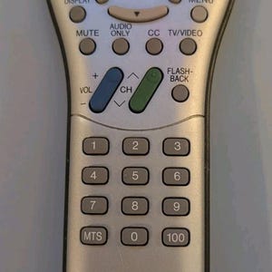 May include: A silver Sharp LCDTV remote control model GA174WJSA with a red power button, a central navigation pad, a blue volume rocker, a green channel rocker, and a numeric keypad. The remote features labeled buttons for sleep, bright, pic.flip, display, menu, mute, audio only, cc, tv/video, flash-back, and mts.