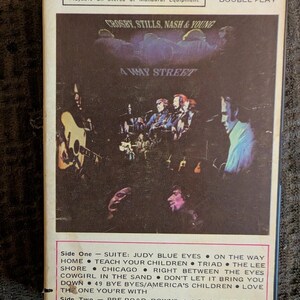 May include: A vintage Crosby, Stills, Nash & Young 4-Way Street cassette tape with a white border. The cover features a dark, moody concert photograph of the band members performing. The tracklist for Side One and Side Two is printed below.