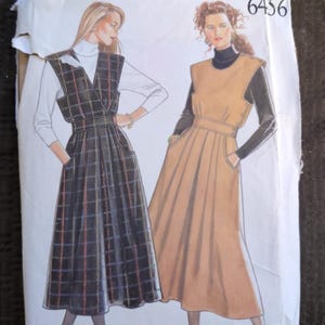 May include: A New Look 6456 sewing pattern envelope featuring illustrations of two sleeveless jumper dresses. One dress is black with a multi-colored plaid pattern, and the other is solid tan. Both dresses have a fitted waist and side pockets.