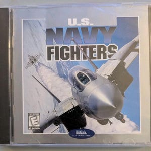May include: A U.S. Navy Fighters video game jewel case featuring a silver fighter jet in flight against a blue sky with clouds. The title U.S. Navy Fighters is printed in bold white text. An ESRB Everyone E rating and Electronic Arts logo are visible.