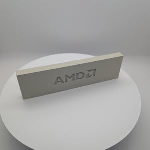 May include: A rectangular, light gray block featuring the AMD logo debossed into its front surface. The object has a smooth, matte finish and clean, sharp edges, presenting a solid, uniform appearance with the brand name clearly visible.
