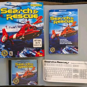 May include: A Search & Rescue 2 PC game set including a large cardboard box, a manual, a CD-ROM case, and a keyboard reference sheet. All items feature a red rescue helicopter flying over water, with the game title printed in yellow and red text.
