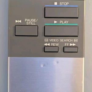 May include: A rectangular Sharp remote control featuring a black top section with Power and TV/VCR buttons, a grey middle section with Stop, Play, Pause/Still, Rewind, and Fast Forward buttons, and a silver metallic bottom panel with the Sharp logo.