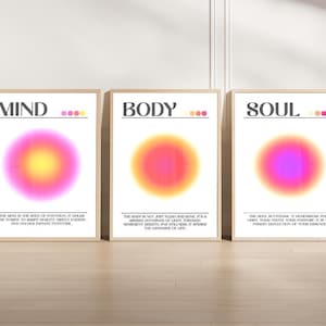 Puede incluir: Tres impresiones artísticas enmarcadas con las palabras "MIND", "BODY" y "SOUL". Cada impresión presenta un diseño circular borroso y colorido en tonos de rosa, amarillo, naranja y morado. Las impresiones se exhiben sobre un suelo de madera clara.