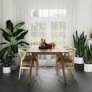 May include: A wooden dining table with four chairs, set in a modern dining room with large windows and potted plants. The table has a light wood finish and the chairs have a natural wood finish.