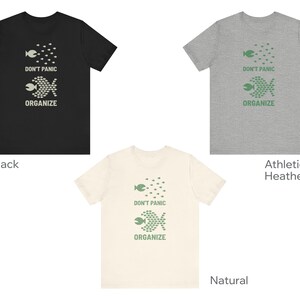 May include: Three t-shirts in black, athletic heather gray, and natural colors. Each shirt features a graphic of fish and the text "DON'T PANIC ORGANIZE" in a contrasting color. The shirts are short-sleeved.