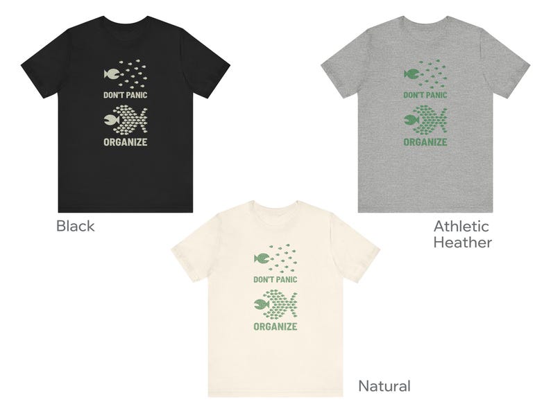 May include: Three t-shirts in black, athletic heather gray, and natural colors. Each shirt features a graphic of fish and the text "DON'T PANIC ORGANIZE" in a contrasting color. The shirts are short-sleeved.