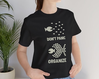 May include: Black t-shirt with a fish graphic and the words "DON'T PANIC ORGANIZE" in a distressed font. The design features two fish, one with scattered smaller fish and the other with organized smaller fish.