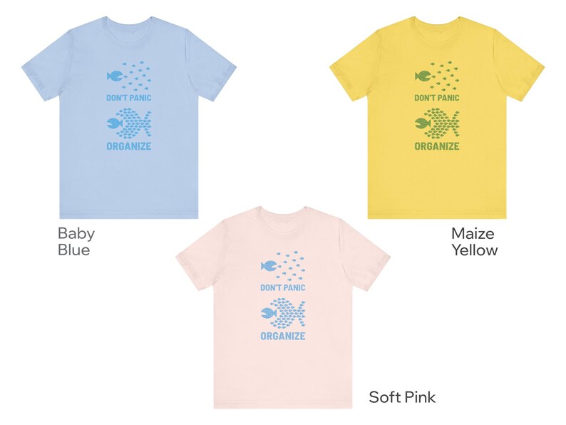 May include: Three t-shirts in baby blue, maize yellow, and soft pink. Each shirt features a graphic of fish and the words "DON'T PANIC ORGANIZE" in a matching color. The shirts are short-sleeved.