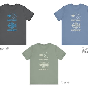 May include: Three t-shirts in asphalt, steel blue, and sage green. Each shirt features a fish graphic with the words "DON'T PANIC ORGANIZE". The shirts are short-sleeved and made of a soft material.