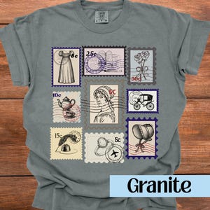 Op de afbeelding: Een grijs Comfort Colors t-shirt met een verzameling vintage postzegelontwerpen. De postzegels tonen verschillende illustraties, waaronder een jurk, rozen, een theepot en een koets. Het woord "Granite" staat onderaan.