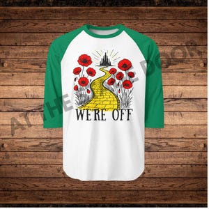 Pode incluir: Camiseta de beisebol branca e verde com um gráfico da estrada de tijolos amarelos, papoulas vermelhas e um castelo. O texto "WE'RE OFF" está impresso abaixo. As mangas são verdes.