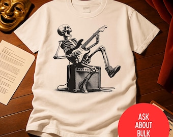 Peut inclure: T-shirt blanc avec une illustration en noir et blanc d'un squelette jouant de la guitare électrique assis sur un amplificateur. Le t-shirt a un col rond classique. Un cercle rouge avec le texte "ASK ABOUT BULK PRICING" est également visible.