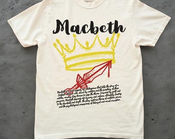 May include: White t-shirt with a yellow crown and a red dagger with a blood drip. The text "Macbeth" is written in black above the crown. The text "Macbeth a dark tragedy by Shakespeare that tells the story of a Scottish general who is driven by ambition and the prophecy of three witches. Macbeth's ambition to seize the throne consumes him by guilt, fear, paranoia, murder, and descent into tyranny and violence. Ultimately leading to his downfall and death. The play explores themes of ambition, power, and the psychological consequences of betrayal and moral corruption." is written in black below the crown.