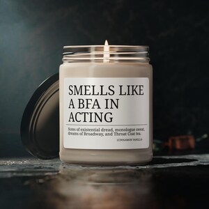 May include: A brown candle with a white label that reads "Smells Like A BFA In Acting". The label also includes the text "Notes of existential dread, monologue sweat, dreams of Broadway, and Throat Coat tea. (Cinnamon Vanilla)"