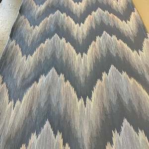 May include: A length of fabric with a repeating chevron pattern. The design features a dark blue background with a textured, layered effect in shades of white, beige, and light pink. The fabric appears to be a medium weight material.