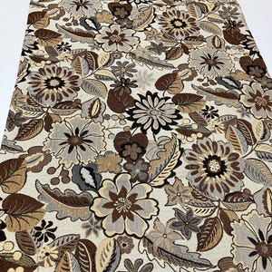 May include: A floral fabric with a repeating pattern of large flowers and leaves in shades of brown, beige, and gray. The fabric has a textured appearance, suitable for upholstery or home decor projects.