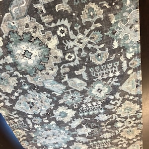 May include: A dark gray fabric with a blue and white patterned design. The pattern features intricate geometric shapes and floral motifs.