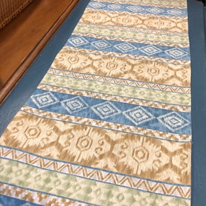 May include: A blue, brown, and green patterned table runner with a geometric design.