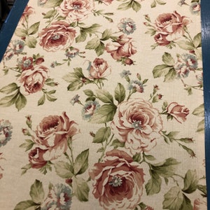 May include: A beige fabric with a floral pattern featuring pink and white roses with green leaves. The fabric has a subtle linen texture.