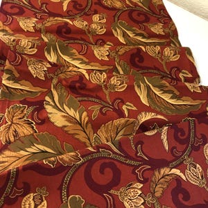 May include: Red fabric with a gold and green floral pattern. The fabric has a paisley-like design with intricate details.