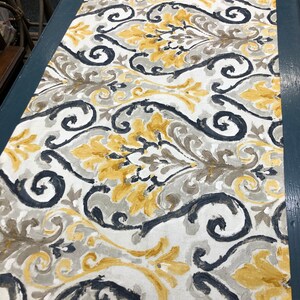 May include: A white fabric with a repeating pattern of black, gray, and yellow swirls and leaves. The fabric has a damask design.