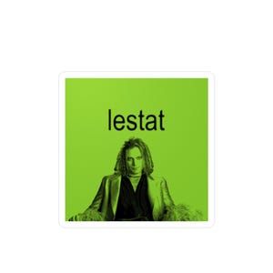 May include: A green background with the word "lestat" in black text. A man with long dark hair is sitting in a chair wearing a black jacket and a black shirt. He is wearing a silver necklace.