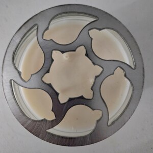 May include: Overhead view of a metal cookie cutter with a circular design and leaf-shaped cutouts. The cutter is filled with a light beige batter, with a central star-shaped cutout. The batter fills the cutouts, ready for baking.