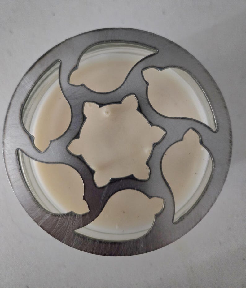 May include: Overhead view of a metal cookie cutter with a circular design and leaf-shaped cutouts. The cutter is filled with a light beige batter, with a central star-shaped cutout. The batter fills the cutouts, ready for baking.