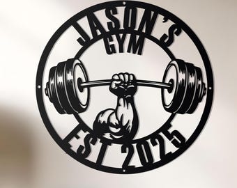 May include: Black metal wall art with the text "JASON'S GYM" in a circular design, featuring a weightlifter lifting a barbell. The text "EST 2025" is below the weightlifter. The art is mounted on a white wall.