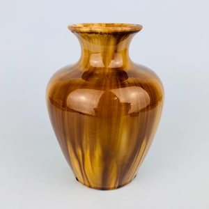 May include: A brown ceramic vase with a glossy finish. The vase has a wide, rounded body that tapers to a narrow neck and flared rim. The color transitions from a light brown at the top to a darker brown at the base.