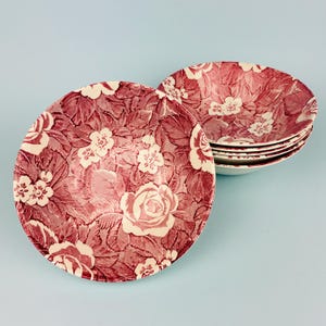 Könnte beinhalten: Ein Set aus sechs Keramikschalen mit floralem Muster. Die Schalen weisen ein bordeauxfarbenes und cremefarbenes Rosen- und Blattdesign auf. Die Schalen sind auf einem hellblauen Hintergrund gestapelt.