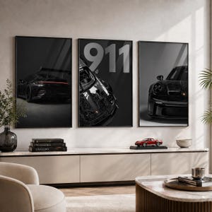 May include: A set of three framed wall art prints featuring black Porsche 911 sports cars. The left print shows the rear, the center print displays a top-down view with the text 911, and the right print shows the front of a black sports car.