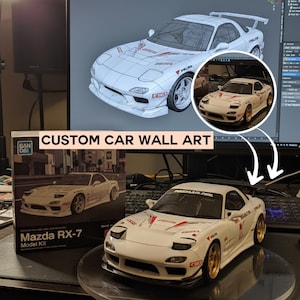 Op de afbeelding: Een wit Mazda RX-7 modelauto met gouden velgen en race-stickers. Het model staat op een transparante standaard, met een doos met het opschrift "Mazda RX-7 Model Kit" en de tekst "CUSTOM CAR WALL ART". Een computerscherm toont een 3D-model van de auto.