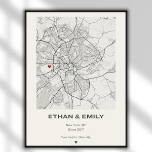 May include: A framed map print featuring a detailed black and white city map with a red heart marker. The text reads "ETHAN & EMILY, New York, NY, Since 2017, Two hearts. One city."
