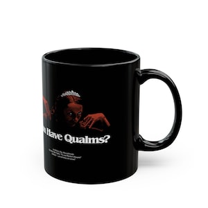 May include: A black ceramic mug featuring a red graphic of a person wearing a tiara with the white text "Do You Have Qualms?" and smaller text below reading "Visit Widow's Bay, Massachusetts. THE NEW YORK TIMES: 'The next Martha's Vineyard.' GOOGLE: '...and definitely not cursed.'"