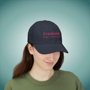 May include: A navy blue baseball cap with the text "Feminist with a to-do list" in pink lettering.
