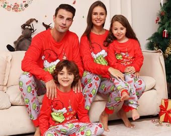 May include: Matching family Christmas pajamas. The red long-sleeved shirts feature a Grinch design with a Santa hat. The gray pants have a Grinch and "Merry" print. The family is sitting on a couch in front of a Christmas tree.