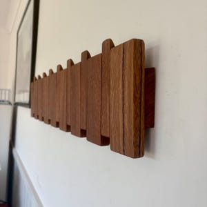 May include: A wall-mounted coat rack constructed from multiple vertical rectangular wooden slats of varying heights. The slats are arranged in a repeating pattern, featuring a rich brown wood grain finish with visible natural textures.