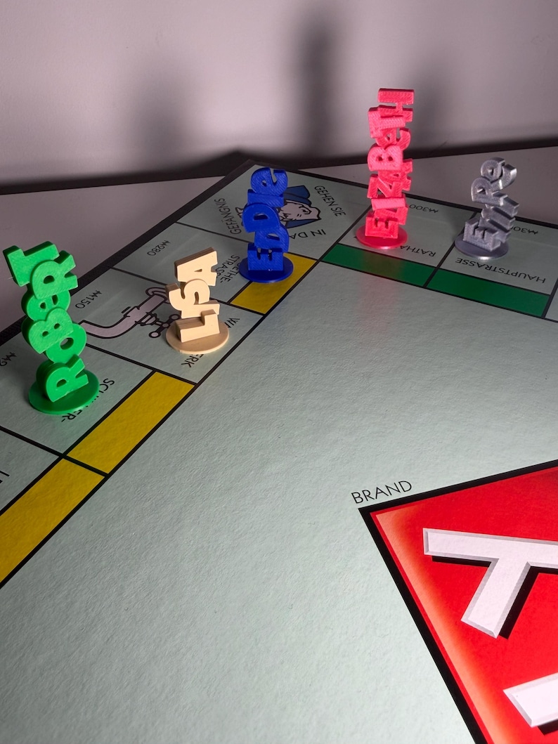 May include: A Monopoly board game with colorful player tokens spelling out names: Robert, Lisa, Edward, Elizabeth, and a silver token. The board features street names and a red corner with the word "BRAND".