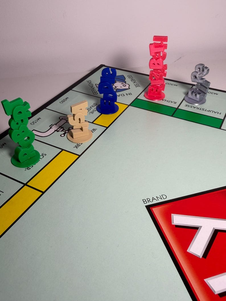 May include: A Monopoly board game with several colorful player tokens. The tokens are in green, tan, blue, red, and gray. The board has various property spaces and the Monopoly logo in the corner.