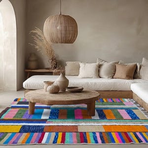 Puede incluir: Una colorida alfombra rectangular con un patrón de rayas en tonos de azul, rosa, naranja, verde y amarillo. La alfombra está colocada en un salón con una mesa de centro de madera y un sofá blanco. Una lámpara colgante tejida cuelga.