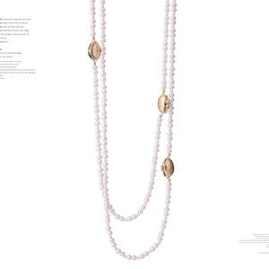 Puede incluir: Dos largos collares de perlas blancas con cierres dorados en forma de concha. Los collares se muestran sobre un fondo blanco. Las perlas son pequeñas y están espaciadas uniformemente, creando un aspecto clásico y elegante.